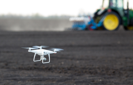 Close up of drone flying above farmland with tractor working in background. High technology innovations for increasing productivity in agricultureの写真素材