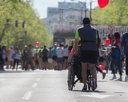 Man pushing wheelchair with disabled girl at street marathon