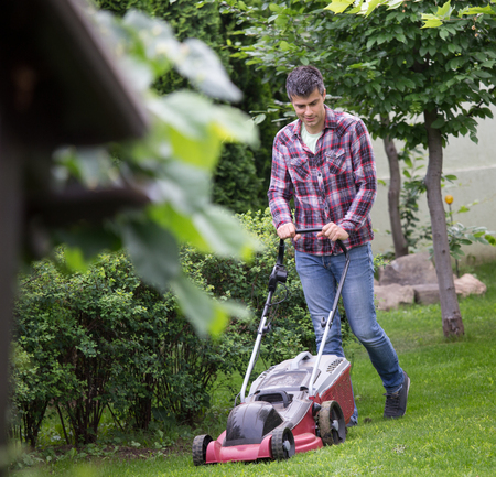 Handsome young man trimming grass with electric mower in backyard in spring