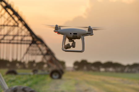 Close up of flying drone above farmland at sunset with irrigation system in background. Agricultural and technology innovations in productionの写真素材