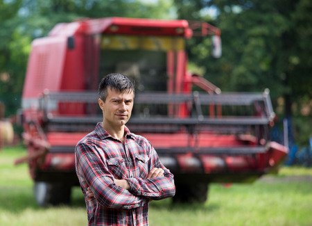 Confident handsome farmer standing with crossed arms in front of combine harvester on farmの写真素材