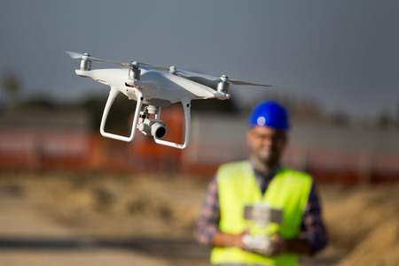 Close up of drone flying at building site and construction worker with remote control in background
