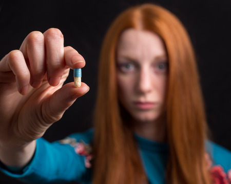 Close up of pill in hand of afraid young woman isolated on black background