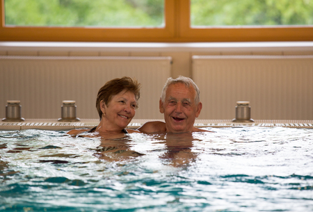 Elderly couple enjoying in indoor pool with hot water in spa resortの写真素材