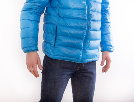 Young man in blue feather jacket and in jeans isolated on white backgroundの写真素材