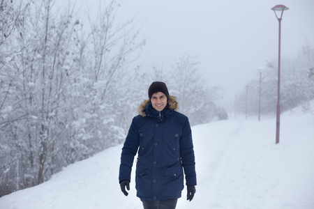 Handsome man walking in park in cold winter day with lot of snow aroundの写真素材