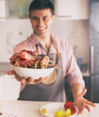 Man holding bowl with fresh meat covered with spices prepared for roasting in kitchen at homeの写真素材