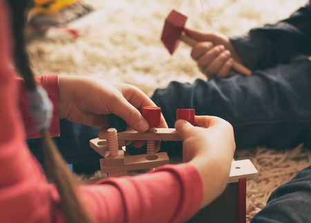 Boy and girl playing with wooden toys on carpet. Close up of little hands practicing motor skills with working toolsの写真素材