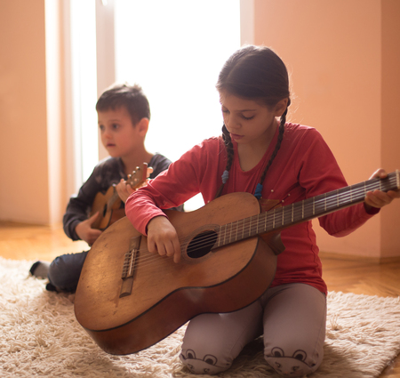 Boy and girl sitting on floor beside window and playing guitarsの写真素材