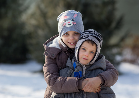 Brother and sister hugging on snow in parkの写真素材