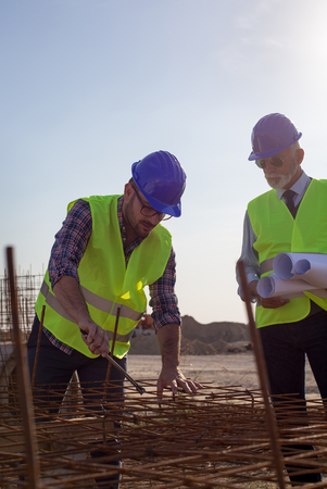 Construction worker with helmet working on reinforcement mesh at building site and engineer talking to himの写真素材