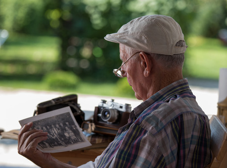 Senior man sitting in garden and looking at old photos. Nostalgia and memories conceptの写真素材