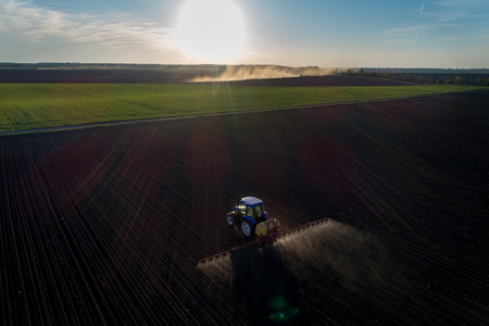 Tractor spraying artificial fertilizer on soil in spring time. Shoot from drone at the eveningの写真素材