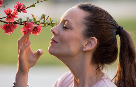 Pretty young woman smelling beautiful red blooming tree in gardenの写真素材