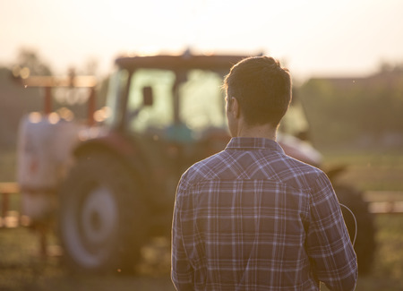 Rear view of handsome farmer standing in front of tractor with sprayer in fieldの写真素材