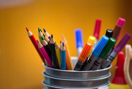 Group of colorful felt pens and wooden crayons in metal box with yeloow background, ready for art...