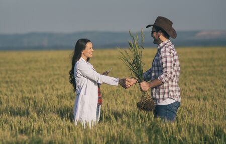 Farmer and woman agronomist in white coat shaking hands in barley field in summer, before harvest