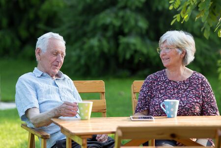 Senior couple sitting at wooden table in garden and drinking tea
