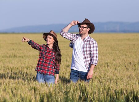Two farmers with hats standing in barley field and looking far away before harvestの写真素材