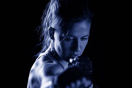Sportive young woman punching and exercising against black backgroundの写真素材