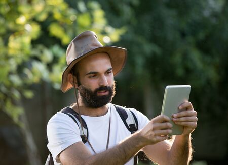 Young attractive man with beard hiking in forest with backpack on shoulders and looking at tabletの写真素材