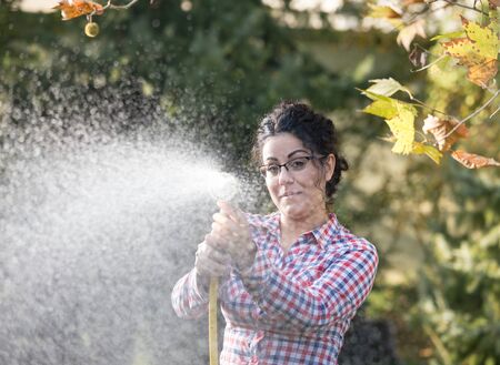 Pretty young girl watering plants in garden with hose in her handsの写真素材