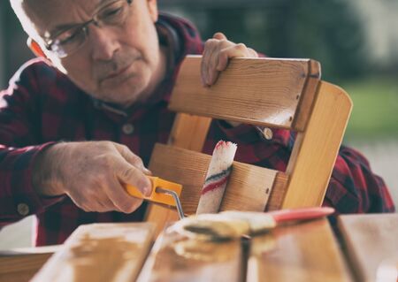 Mature man varnishing chair with lacquer roll in gardenの写真素材