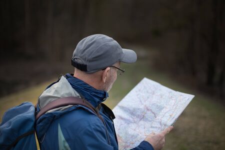 Mature hiker taking break and looking at map iin forest