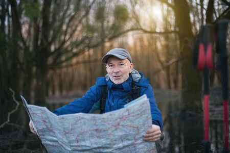 Mature hiker taking break and looking at map in forestの写真素材