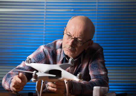Old man repairing drone with screwdriver on desk in the officeの写真素材