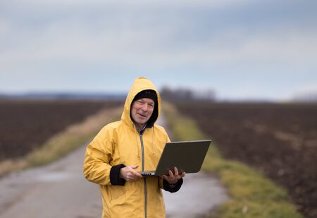 Mature farmer with laptop standing in field in winter time