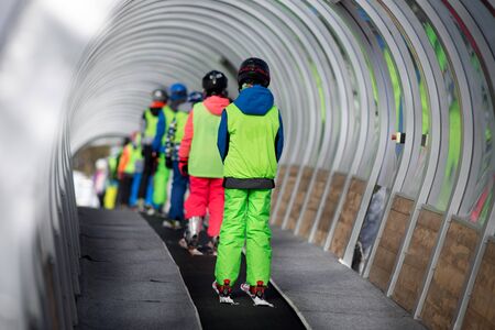 Rear view of children in ski school lifting the slope with conveyor belt in tunnel