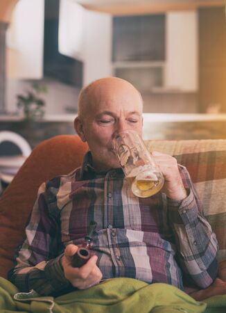 Man sitting in armchair at home, drinking beer and smoking pipeの写真素材