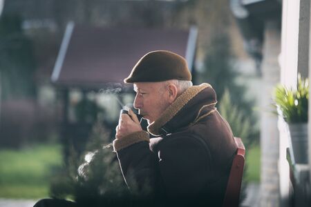Senior man drinking coffee in park on cold winter dayの写真素材