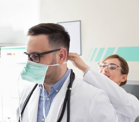Pretty nurse helping handsome doctor to tie protective mask in ambulanceの写真素材