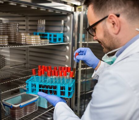 Biologist in white coat and with protective gloves taking out samples from modern incubator