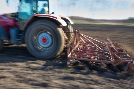 Panning technique of tractor harrowing soil in field in early spring timeの写真素材