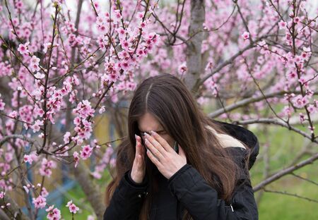 Pretty girl sneezing beside blooming tree. Spring allergy conceptの写真素材