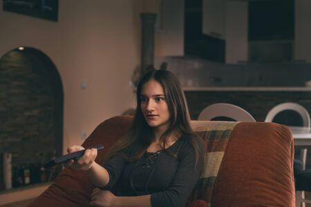 Excited teenage girl holding remote control and watching movie on tv in living roomの写真素材