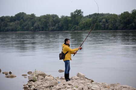 Handsome angler fishing on river coast with stone in spring time