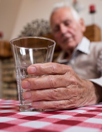 Close up of old man's hand holding glass of water at tableの写真素材