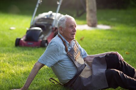 Senior man resting on lawn after mowing grass in courtyard