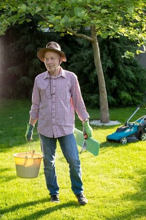 Portrait of mature man with garden tools in backyard and mower in backgroundの写真素材