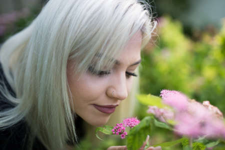 Portrait of pretty blond teenage girl smelling pink flowers in garden