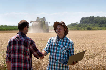 Two farmers shaking hands in wheat field during harvest, with combine harvester in backgroundの写真素材