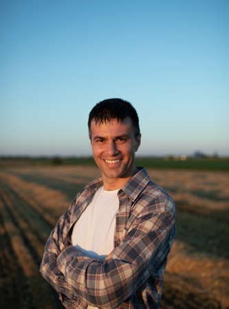 Handsome farmer with crossed arms standing in field during harvestの写真素材