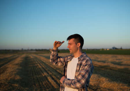 Handsome farmer standing in field during harvest, holding hand above eyes to block sunの写真素材