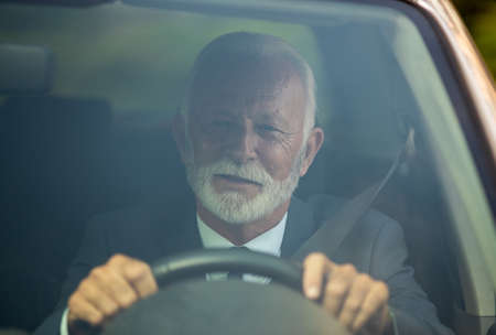 Senior man in business suit driving car. Shoot from windshieldの写真素材