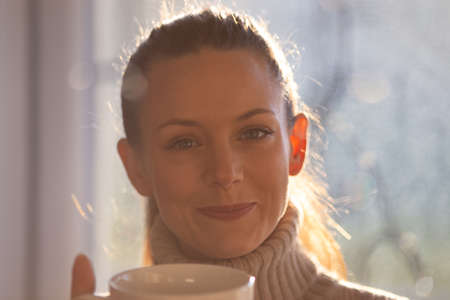 Portrait of pretty girl drinking hot coffee beside window at sunrise