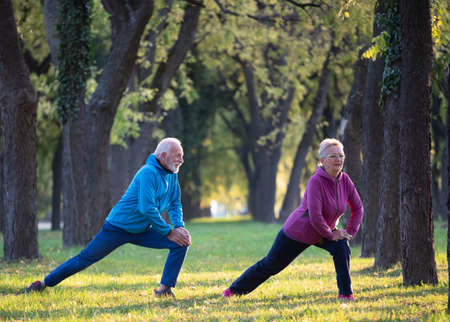 Senior couple stretching legs and warming up for exercise and jogging in park on sunny autumn day